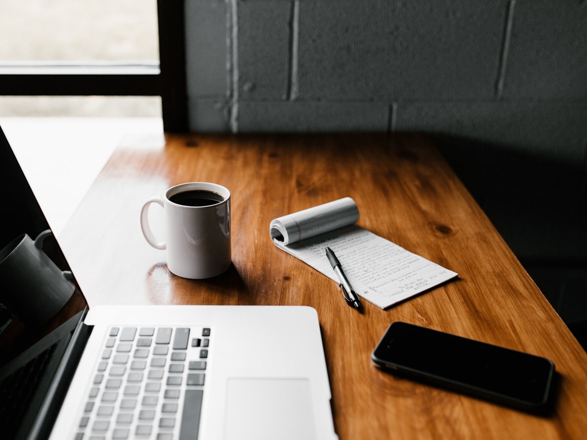 A laptop, notebook, and coffee on a content writer's desk
